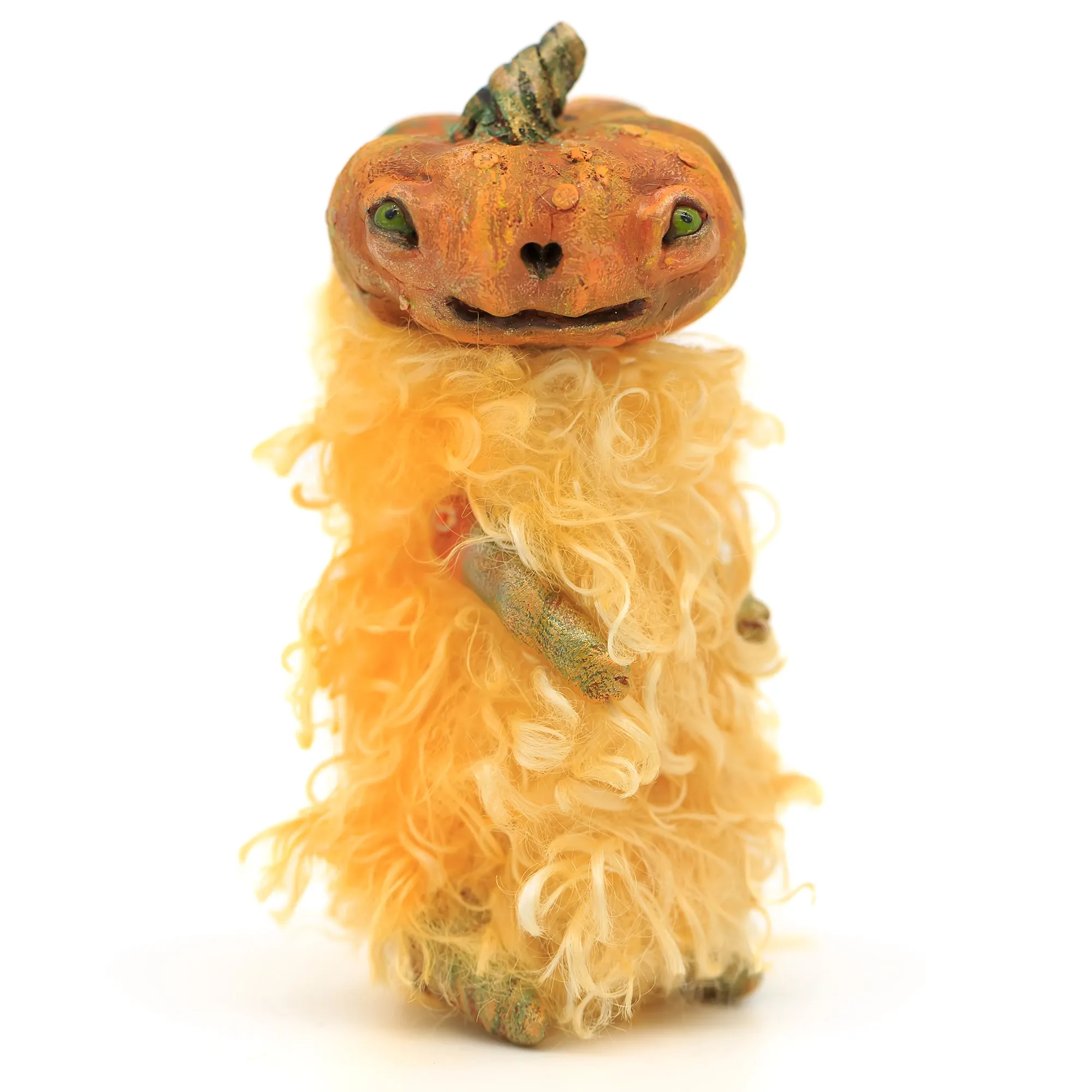 Pumpkin art doll looking directly at the viewer. It has sculpted out of polymer clay head and four limbs. Its body is made with light yellow faux fur fabric. It has a wavy texture and resembles straw bale. The doll can sit upright on its back limbs, but cannot stand on its own.
